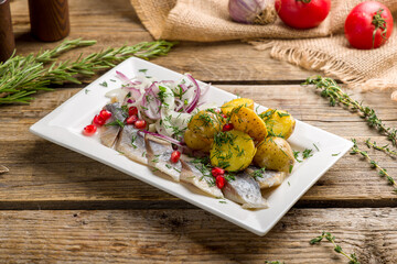 Herring with potatoes and red onion on white plate on wooden table
