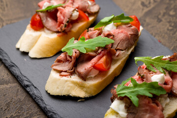 Bruschetta with roast beef, tomatoes and aragula on black stone