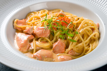 Spaghetti pasta with salmon and red caviar with parmesan on white plate on dark concrete table macro close up