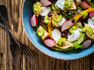 Roast chicken salad with radish, cucumber, yellow pepper and leafy greens vegetables on wooden table
