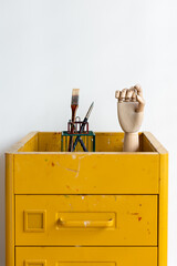Hand mannequin and paintbrush on yellow pedestal. Arts and crafts.