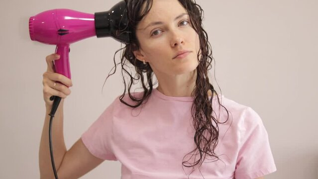 A young woman is styling her curly, wavy hair with a special diffuser hair dryer attachment.