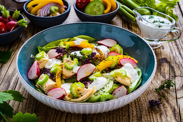 Roast chicken salad with radish, cucumber, yellow pepper and leafy greens vegetables on wooden table

