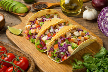 Chicken tacos with avocado, salsa, red cabbage, tomatoes and lime on an old rustic wooden table. - 518962034