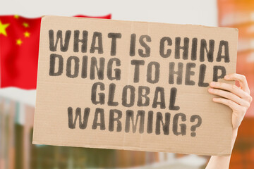 The question " What is China doing to help global warming? " on a banner in the man's hand with a blurred Chinese flag in the background. Desert. Downtown. Change. Future. Warning. Outdoor. Summer