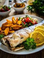 Fried perch with boiled potatoes, lemon and fresh vegetable salad served on wooden table
