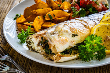Fried perch with boiled potatoes, lemon and fresh vegetable salad served on wooden table
