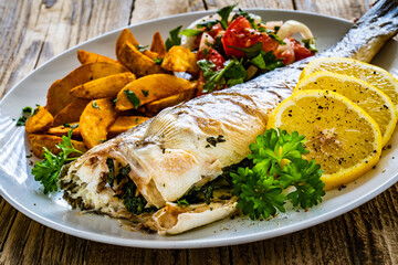 Fried perch with boiled potatoes, lemon and fresh vegetable salad served on wooden table
