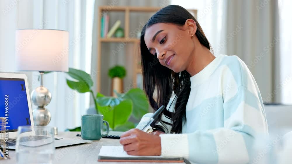 Poster Young happy student writing and planning in a book while studying at a desk at home. One female Indian woman doing an assignment and taking notes in a notebook while preparing for an exam alone