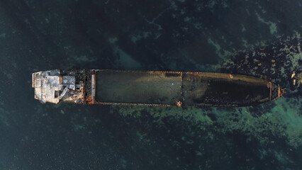Aerial top view for wrecked ship along the rocky coast in blue water. Shot. Old sunk boat near sea...