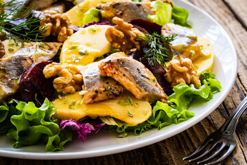 Marinated herrings with roasted beetroots, apple, walnuts  and fresh vegetable leaves on wooden...