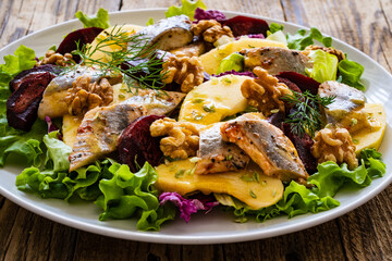 Marinated herrings with roasted beetroots, apple, walnuts  and fresh vegetable leaves on wooden...