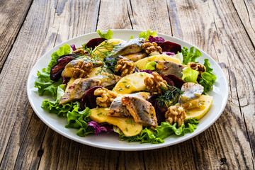 Marinated herrings with roasted beetroots, apple, walnuts  and fresh vegetable leaves on wooden...