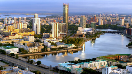 Fototapeta na wymiar Yekaterinburg, Russia, aerial view of the city with the Iset tower and the river with embankment. Stock footage. Drone view of the city center with wide road and many houses.