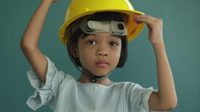 Portrait Thai Asian kid girl, aged 4 to 6 years old, cute and healthy, she is learning and practicing to wear a yellow helmet. to prevent things from falling on the head and shockproof