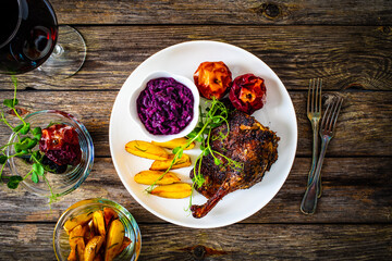 Roast duck thigh with, baked potatoes, fruits and and red cabbage on wooden table
