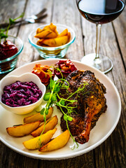 Roast duck thigh with, baked potatoes, fruits and and red cabbage on wooden table
