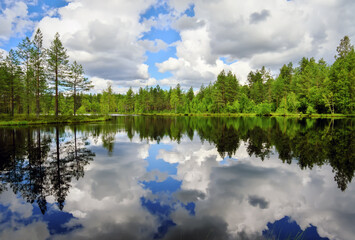 Quiet smooth beautiful lake in Karelia. Cloudy blue sky. Forest with trees and fir-trees.