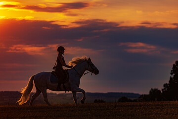 young woman galloping on horseback during sunset