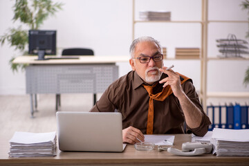 Old male employee smoking cigarette at workplace