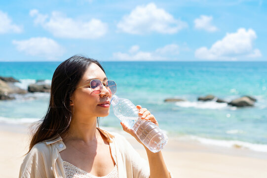 Woman drinking water from plastic bottle in summer sunlight by the sea. Concept of health and freshness, thirst, rehydration concept. Closeup, copy space