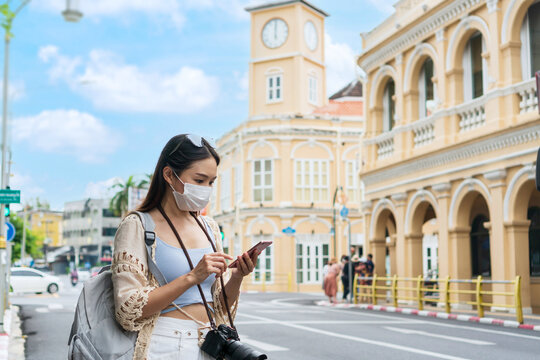 Happy Asian traveler female looking a map on mobile phone while walking at old town Phuket, Thailand. Travel alone, Summer and holiday concept
