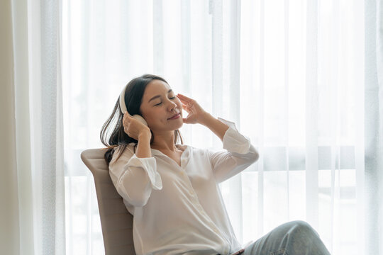 Young smiling Asian woman sitting  and listening music. Young brunette girl relaxing at home in a leisure time..Copy space