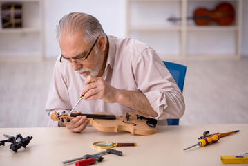 Old male repairman repairing musical instruments at workshop