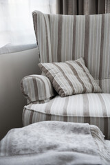 Gray wing chair, puff and blanket placed next to a window inside a house. Furniture for decorating. Color combination.