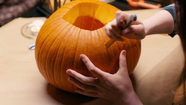 Preparing pumpkin for Halloween. Woman sitting and carving with knife face details of halloween Jack O Lantern pumpkin at home for her family.