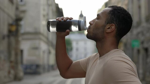 Side view african american runner drinking water from the sport bottle after the scamper. Man feels thirsty after running from sport bottle. Sport and healthy lifestyle concept.