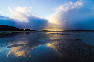 Reflection on the beach surface of a storm cloud system moving away from Red Wharf Bay, Gwynedd, Anglesey, North Wales