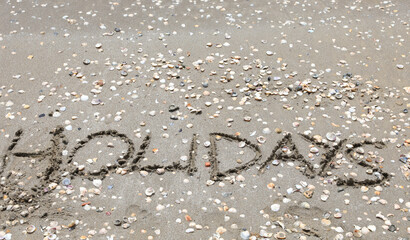 large text with the word HOLIDAYS in capital letters on the sand of the sandy beach by trhe sea