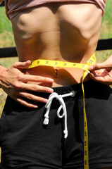 young anorexic teen girl with eating disorders very skinny while measuring her waist using a flexible measuring tape - obrazy, fototapety, plakaty