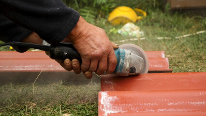 Roofer using an angle grinder machine to cut a roof tile of red color. Stock footage. Close up of male worker hands cutting a roof tile with a professional saw.
