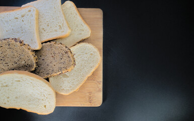 Various types of bread baked and cut on a wooden board on a black background. With space for text