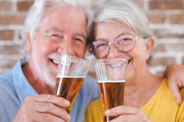 Defocused senior smiling couple toasting with a glass of blonde beer