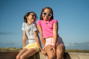 Best friends sitting near each other at the wooden fence and smiling while walking