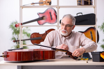 Old male repairman repairing musical instruments at workplace