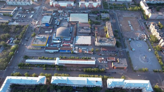 Aerial view from a drone of the small town of Balkhash on the shore of the lake. Low houses are painted in different colors, wide alleys, green trees grow. Cars are driving along the road. The clouds