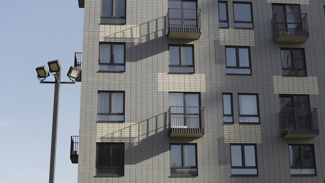 Bottom view of residential new building made of white bricks. Action. Fragment of a white brick new apartment house with balconies and street lanterns against a clear sky.