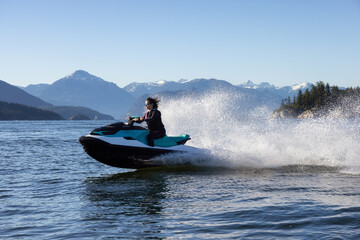 Fototapeta premium Adventurous Caucasian Woman on Sea-Doo riding in the Ocean. Lighthouse park in background. West Vancouver, British Columbia, Canada.