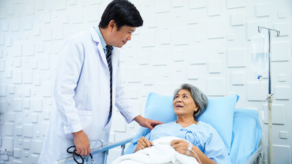 Male doctor came to inquire about the symptoms of an elderly female patient lying in bed receiving saline in the patient's room. Elderly female patient responds Male doctor with a smiling face.