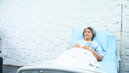 Elderly woman patient lying in bed receiving saline in the patient room have a worried face and...