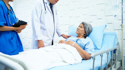 Obraz premium Specialist male doctor and his assistant came in to inquire about the symptoms of a female patient after receiving treatment. Female patient lying in bed responding to the doctor with a carefree face.