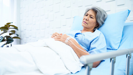 Fototapeta premium Elderly woman patient lying in bed receiving saline in the patient room have a worried face and weary of her sickness. Female patient lying in bed There is hope that the treatment will improve.
