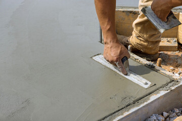 A masonry worker is smoothing the plastering concrete to cement floor while holding steel trowel in his hand