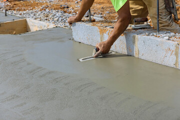 There is a masonry worker holding a steel trowel smoothing plastering concrete to a cement floor with a steel trowel