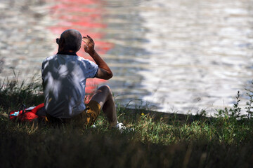 A man sits in the shadow under a tree while he turns his head to the left side.