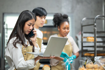 Young asian male and African female in apron using laptop and talking to clients on the phone by workplace.Group of friend  seller browsing online on cellphone. Bakery shop Business  concept. 